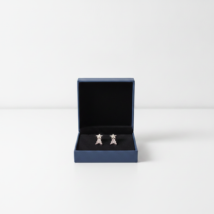 A pair of silver-toned earrings displayed inside an open dark blue jewelry box with a black velvet lining, set against a clean white background.