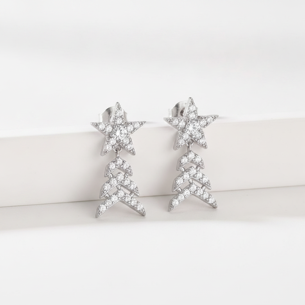 A pair of silver-toned dangle earrings featuring a star-shaped top set with clear crystals and a dangling chevron tree design below, displayed on a clean white surface.
