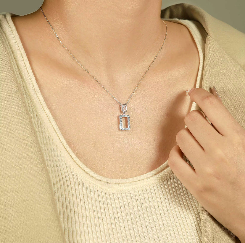 Necklace with a rectangular pendant worn by a person in a beige top.