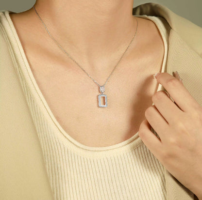 Necklace with a rectangular pendant worn by a person in a beige top.